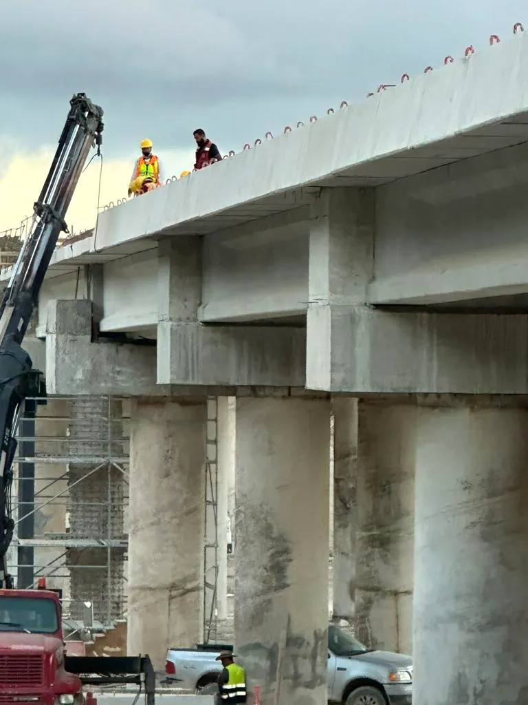 Viaducto de concreto en construcción con personal sobre la losa y grúa de apoyo